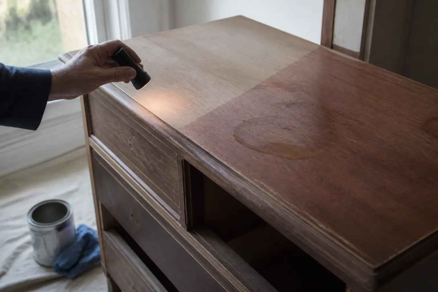 Peinture meuble sans poncer : buffet en bois inspecté avant peinture, main avec lampe, vernis usé et tache visibles