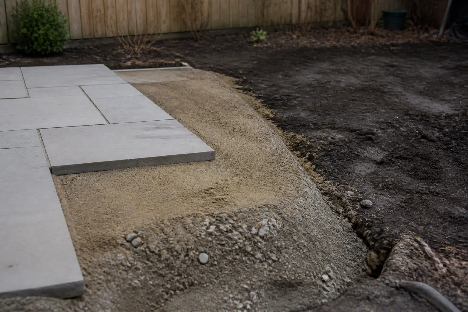 Pose dalle sur sable sur terrasse en chantier, sol stable, sable compacté et dalles posées, terrain humide en bordure.