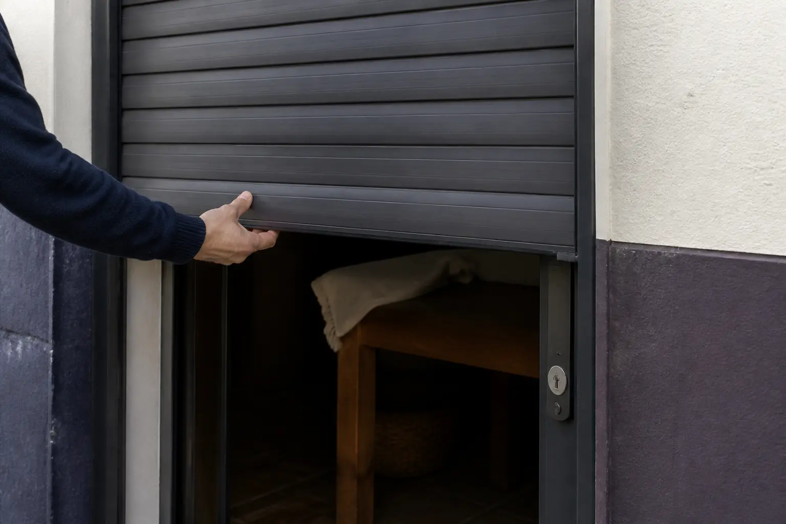 Volet roulant tirage direct sur porte de service, main levant le tablier en aluminium mat, extérieur résidentiel réel.