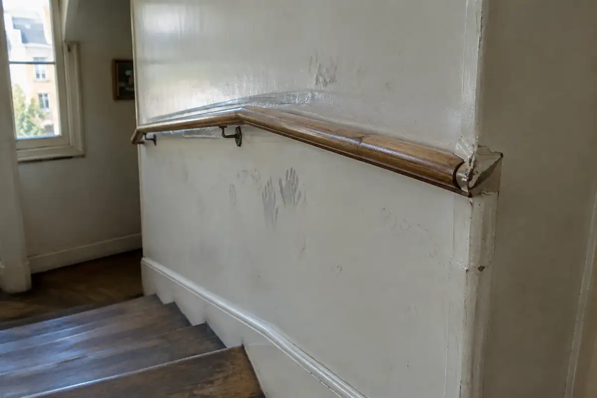 Traces de mains et frottements sur une peinture claire le long d'une main courante d'escalier
