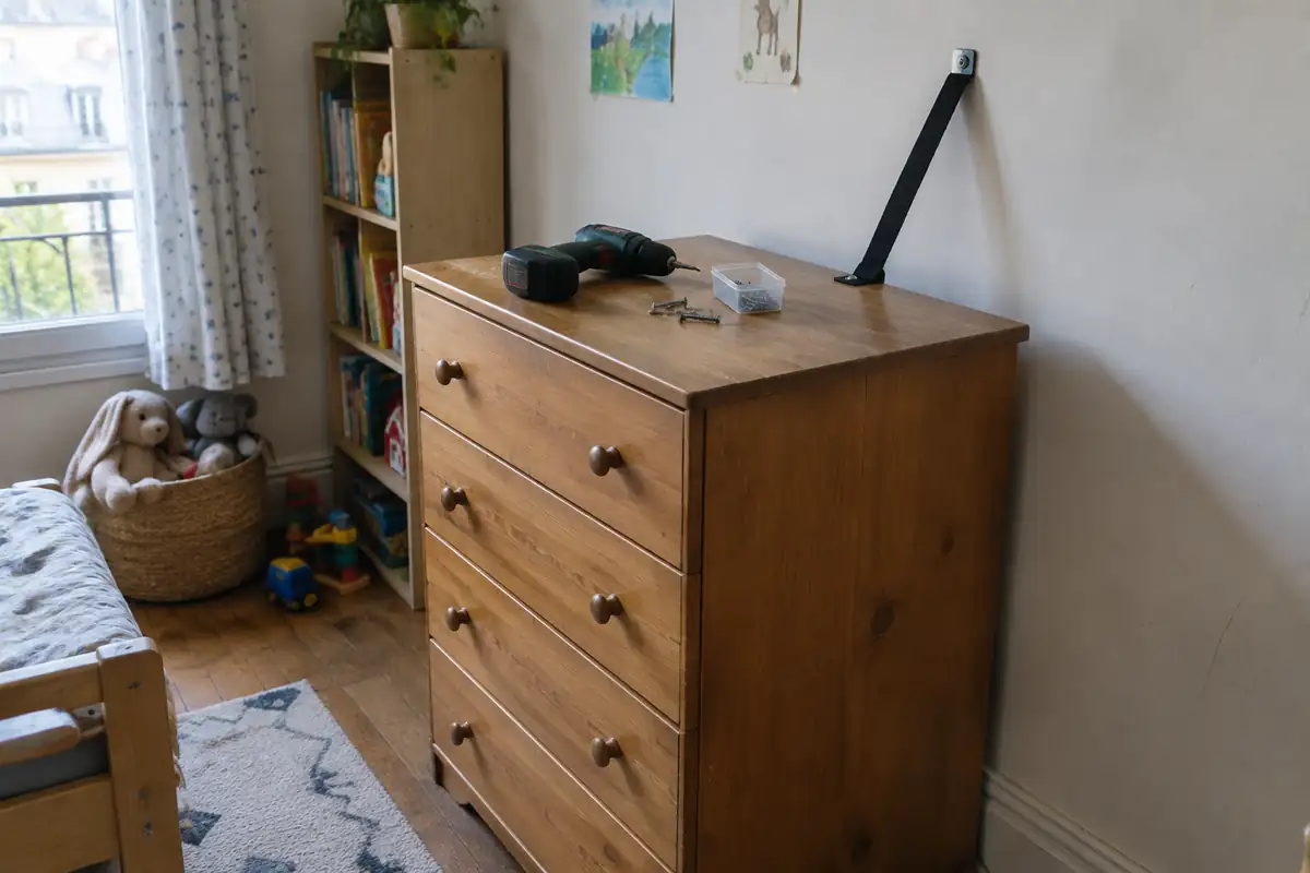 Commode en bois fixée au mur par une sangle vissée, avec une perceuse posée dessus