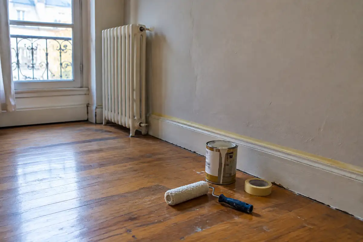 Petit pot de peinture, rouleau et ruban de masquage posés au pied d'un mur
